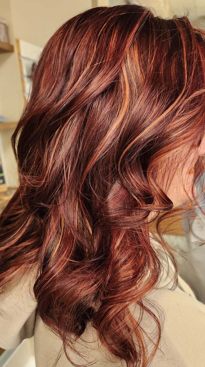 Rich auburn brown wavy hair featuring vibrant copper and warm red dimensional balayage highlights, styled at Silhouette Spa hair salon.