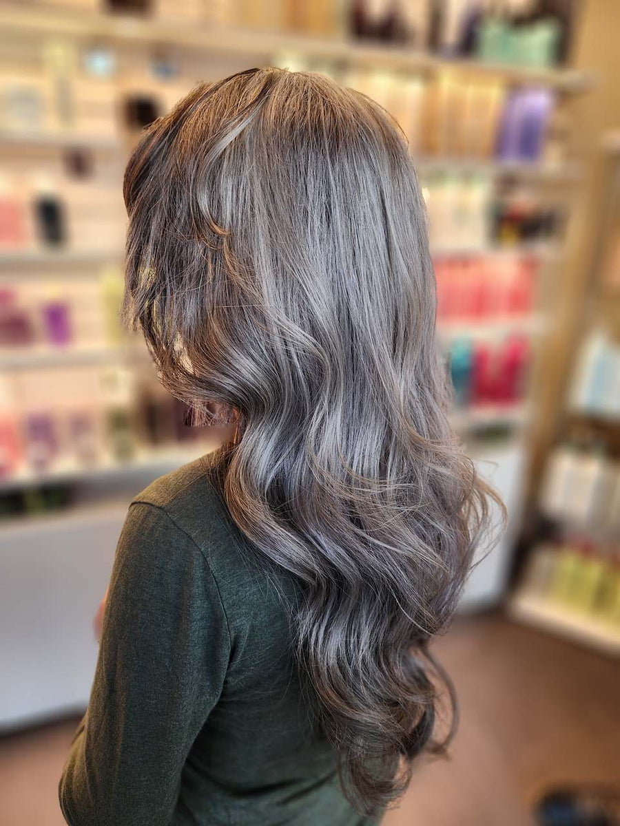 Long beach waves featuring a cool-toned ash brown base with silver blonde and charcoal balayage highlights, done at Silhouette Spa hair salon.