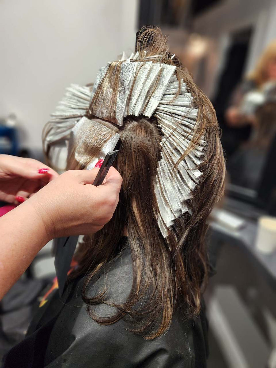 Professional hairstylist applying foil highlights and color treatment to long brunette hair at Silhouette Spa hair salon.
